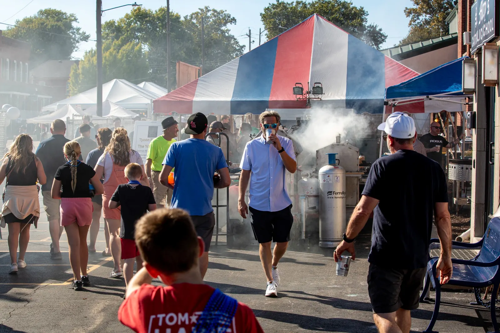 Festival crowd walking through food tents and smoke from grills